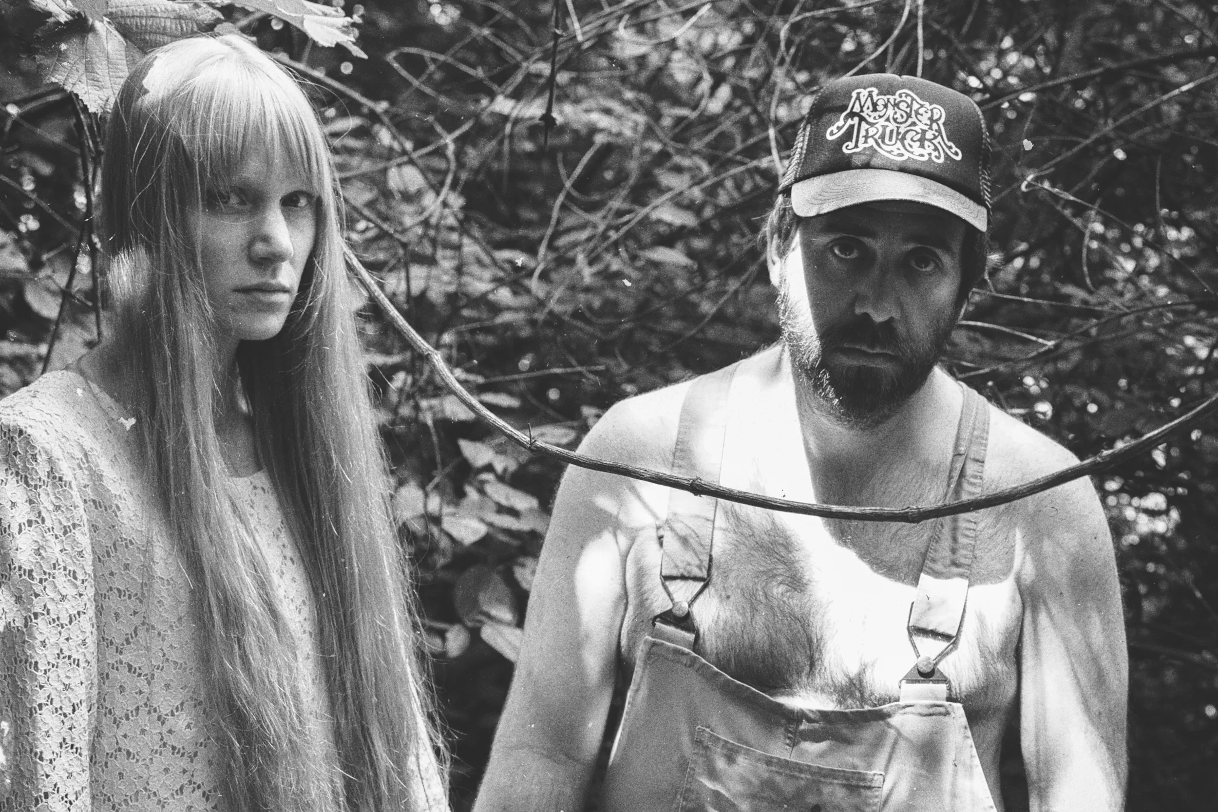 Black and white forest portrait of a couple, man wearing a Monster Truck cap.